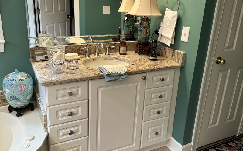 Elegant master bathroom vanity with cream cabinetry, granite countertop, and teal accent walls accented with framed Asian artwork.