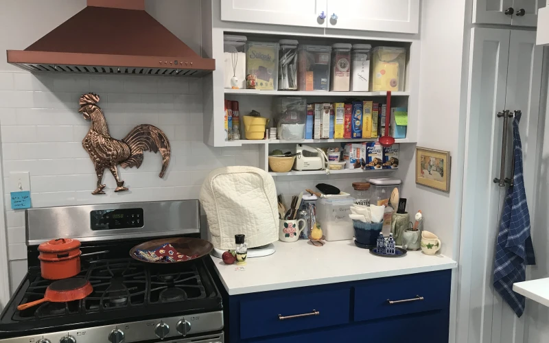Modern kitchen renovation featuring navy blue cabinetry with copper hardware, stainless steel appliances, white subway tile backsplash, and open shelving with decorative cookware and pantry items.