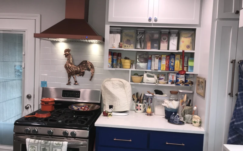 Modern kitchen remodel featuring navy blue lower cabinets, white countertops, open shelving with organized storage, stainless steel gas range with copper hood, and subway tile backsplash.