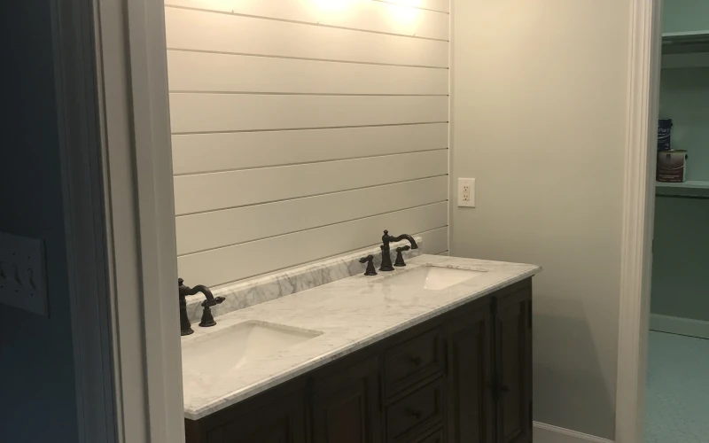 Modern bathroom vanity with dark cabinetry, marble countertop, dual faucets, and five black gooseneck sconces above shiplap accent wall.